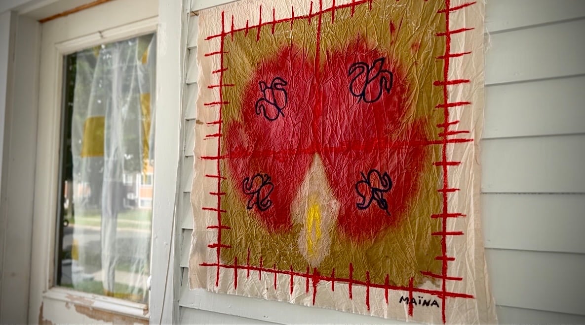 A mixed media artwork with red and gold tones and stitched red borders displayed on a white wall.