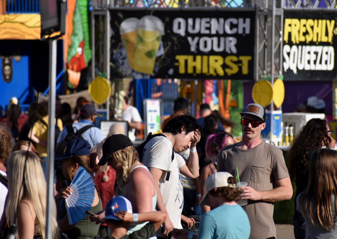 A man wipes sweat from his brow in sunlight as crowds of people attend the midway of a summer fair in Medicine Hat, Alta.