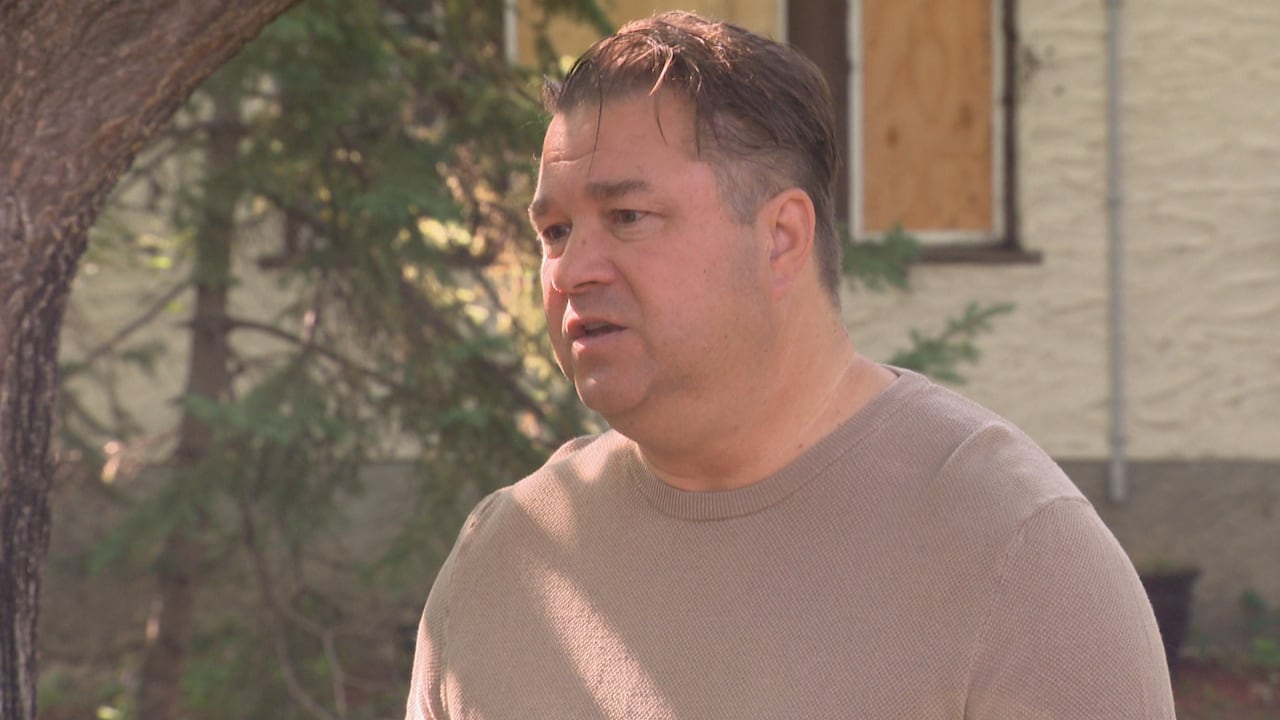 A man in A T-shirt speaks outside a house.