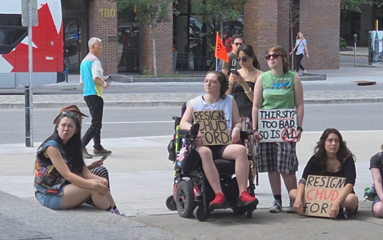 People holding signs protesting Premier Doug Ford on a summer day.