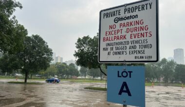 A sign in the foreground says "No parking except during ballpark events," with a puddle-filled parking lot in the background