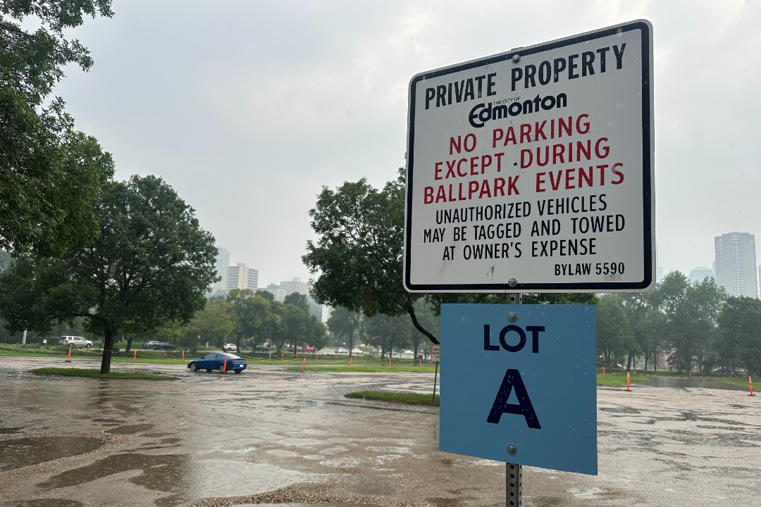 A sign in the foreground says "No parking except during ballpark events," with a puddle-filled parking lot in the background