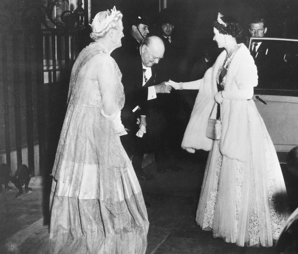 A person leans down to kiss another person's hand as others look on.