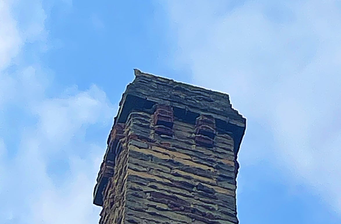 A bird sits on the edge of a chimney set against a blue sky.