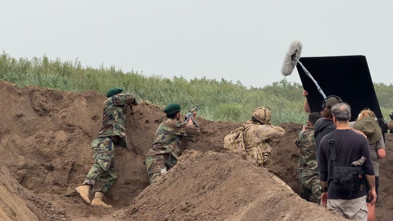 Three actors dressed in Afghan military uniforms and one dressed in a Canadian uniform are shooting over a dirt trench.