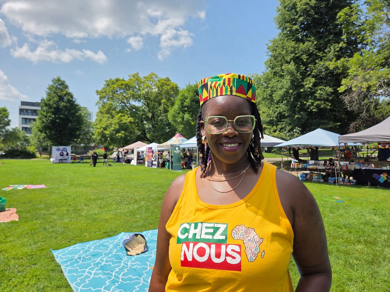A black woman stands in a park on a sunny day and smiles at the camera.