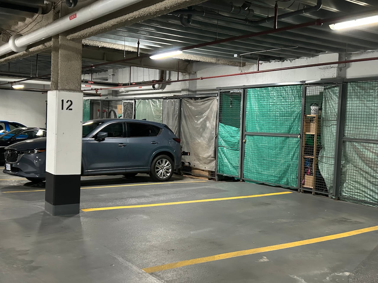 An underground parking lot. At the end of each spot are wire-mesh cages draped in tarps.