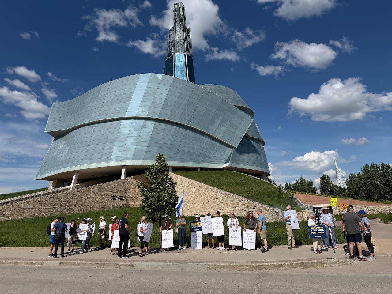 A line of people carrying placards stands in front of the Canadian Museum for Human Rights.