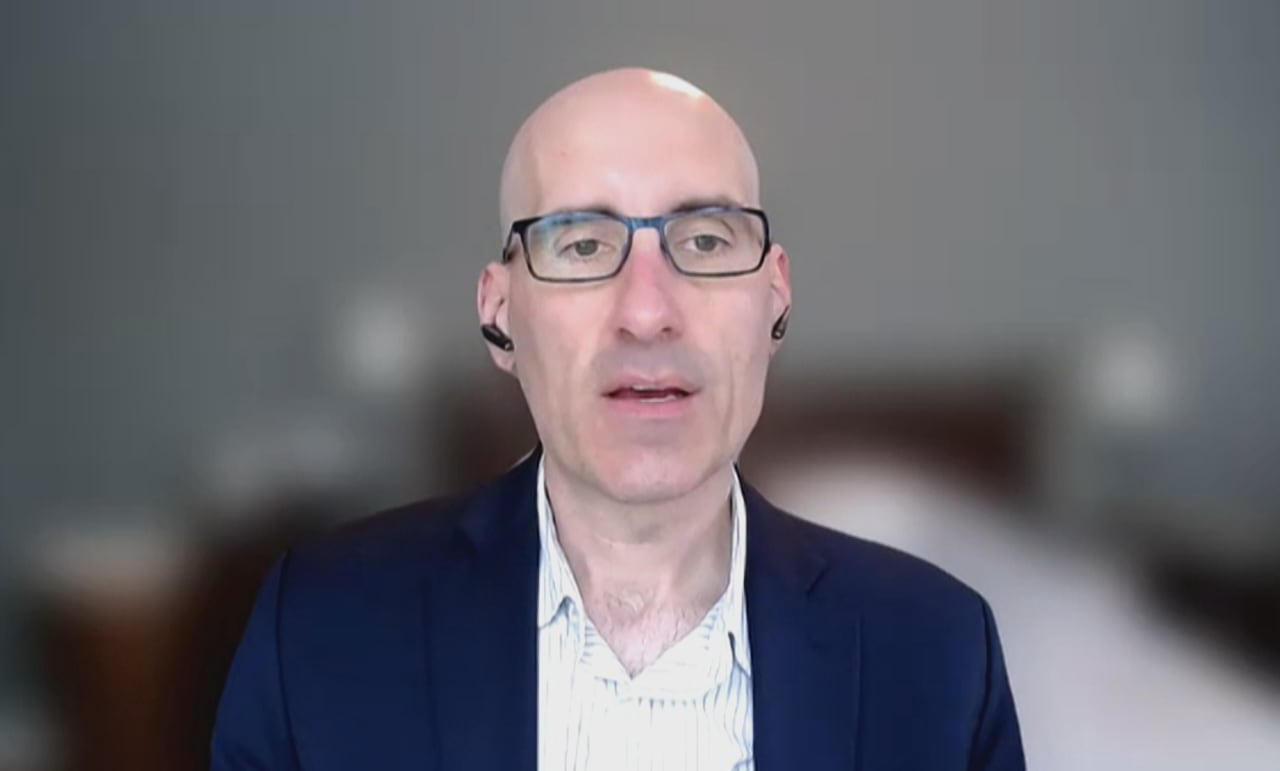A screengrab shows a man wearing a blue blazer and a white button up shirt.