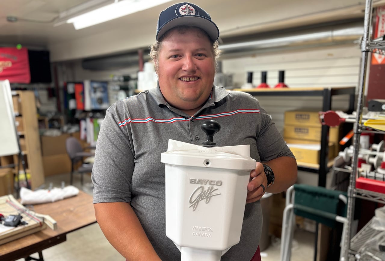 Andrew Hunt is smiling and standing inside his shop while holding a white golf ball washer.
