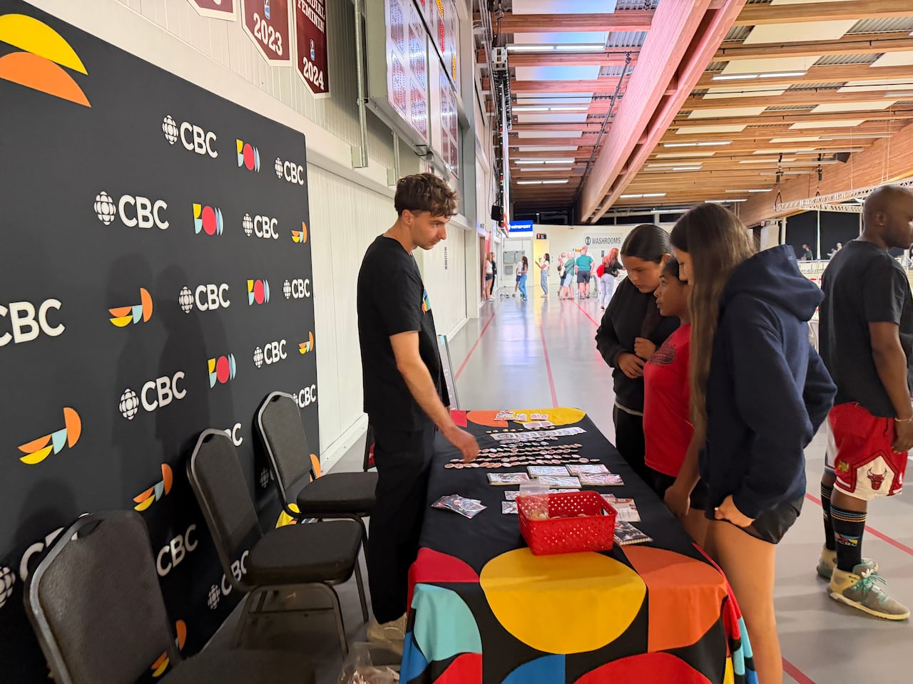 Three young people speak with an adult at a table decorated with CBC logos.