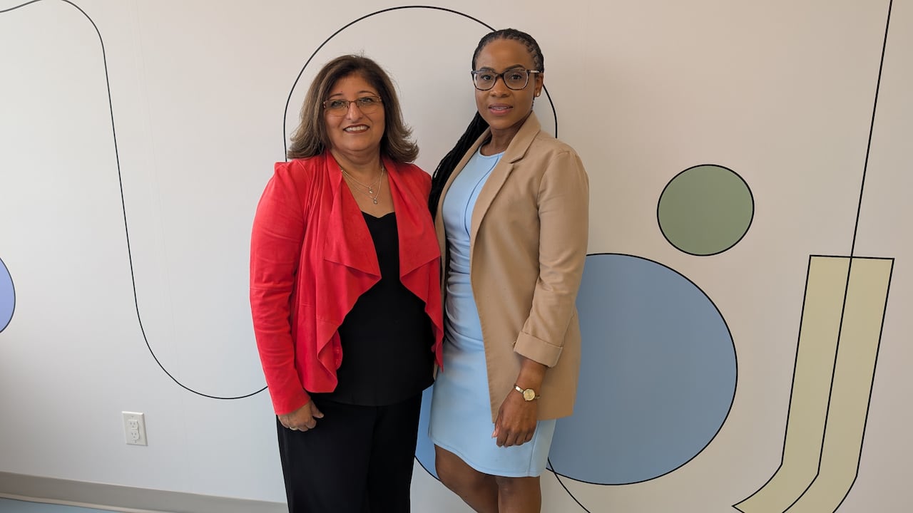 Two women poise in front of a colourful wall inside the Safe Centre of Peel.