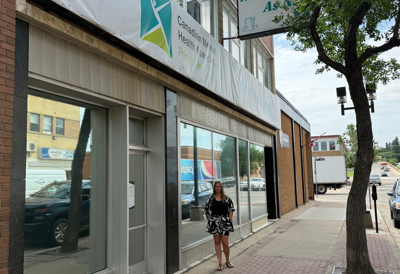 A woman with long brown hair stand in front of the store from of the Canadian Mental Health Association building in downtown Prince Albert.