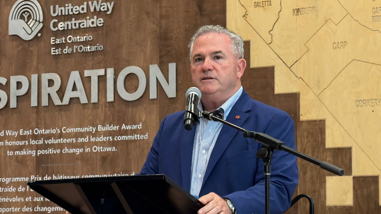 A man with short grey hair, wearing a blue suit, stands behind a podium.