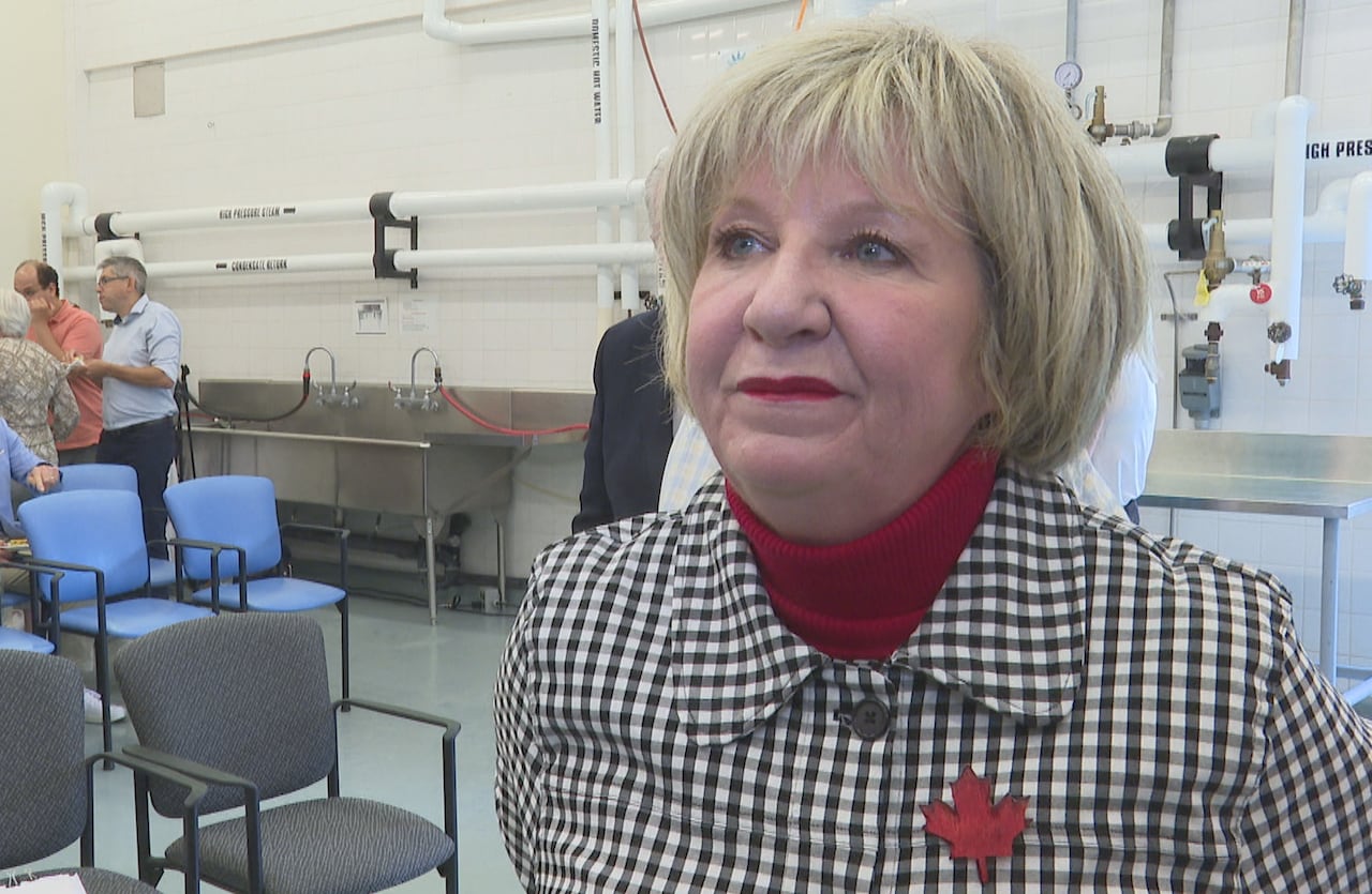 Close-up portrait of a woman wearing a black-and-white houndstooth jacket with a red maple leaf pin in a room with blue chairs.