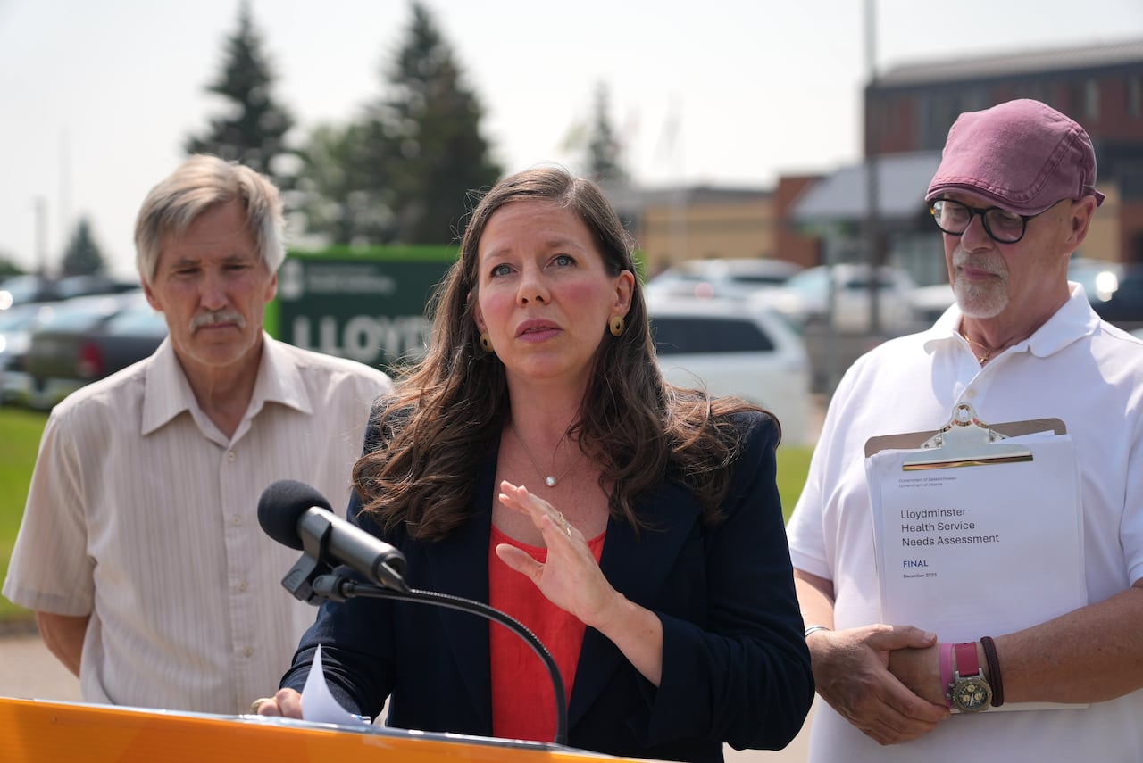 A woman flanked by two men stand at a podium during an outdoor press conference.