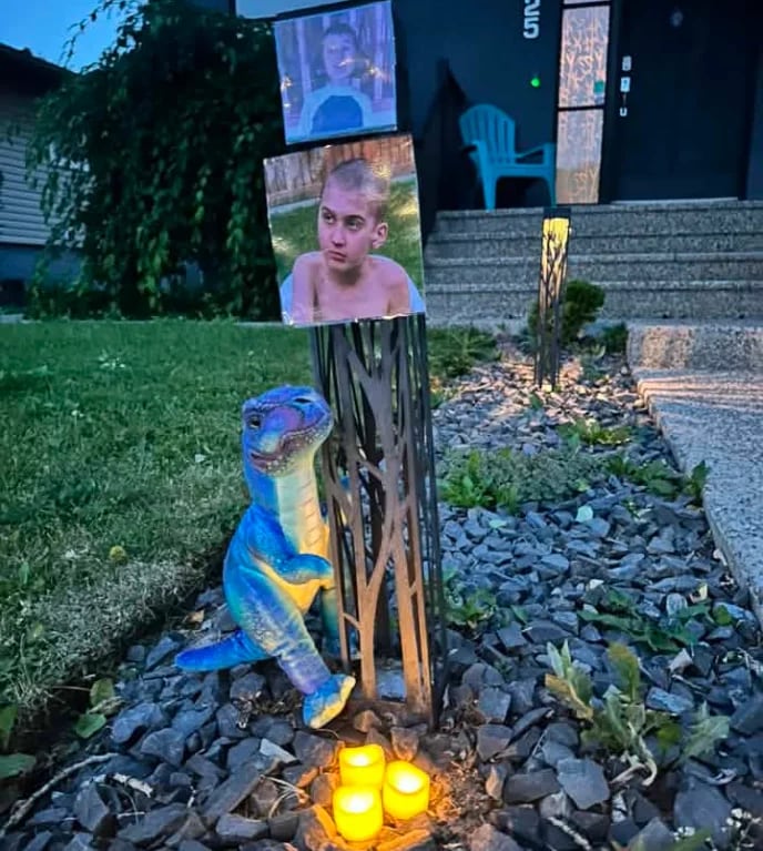 A photo of a young boy attached to a post, with a candle and a toy dinosaur beneath