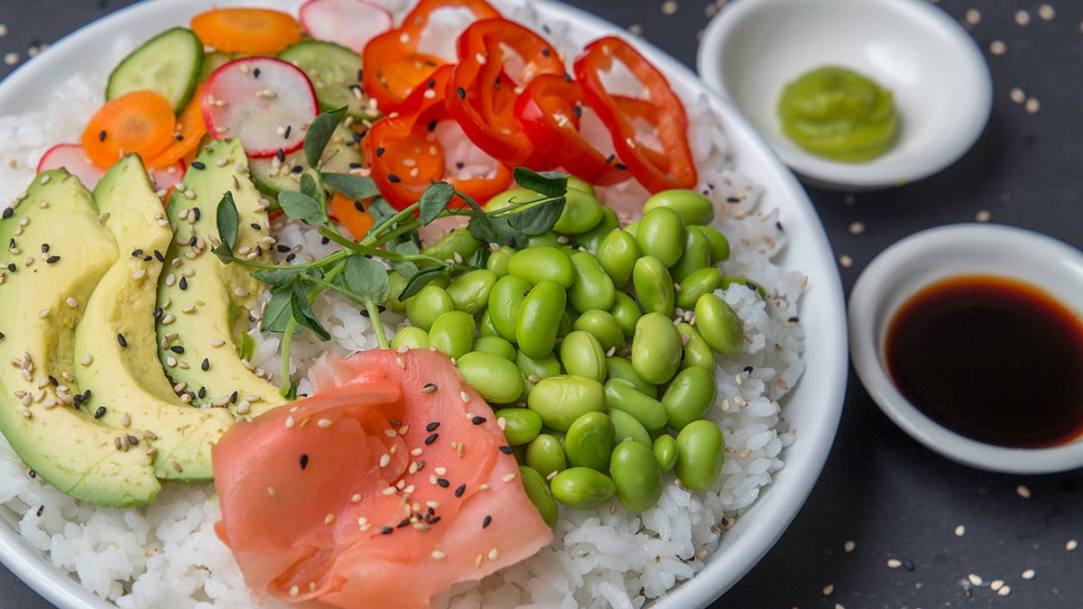 Closeup on a bowl of rice topped with avocado, edamame and ginger.