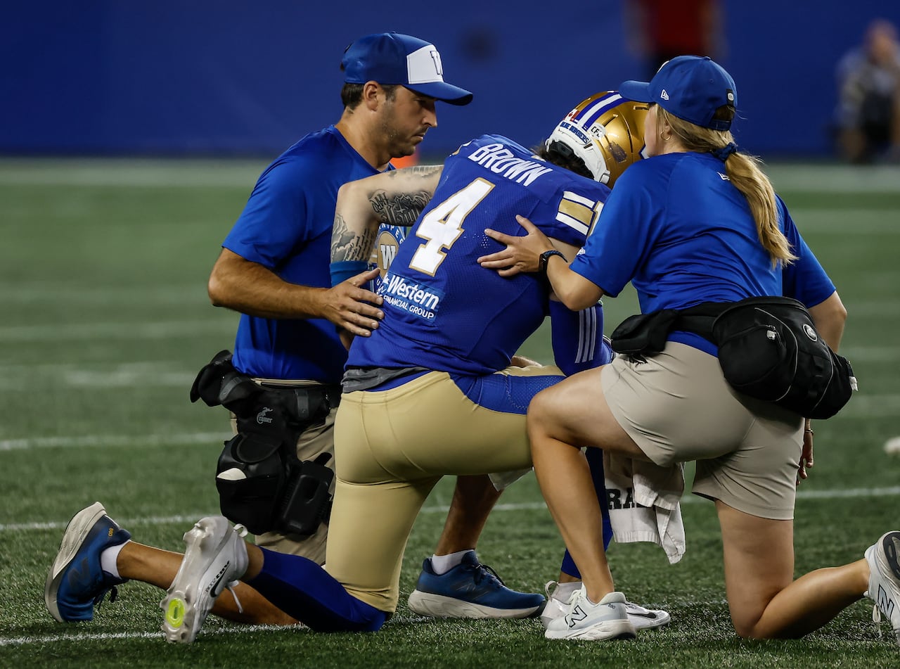 A Bomber player takes a knee while being tended to by two training staff.