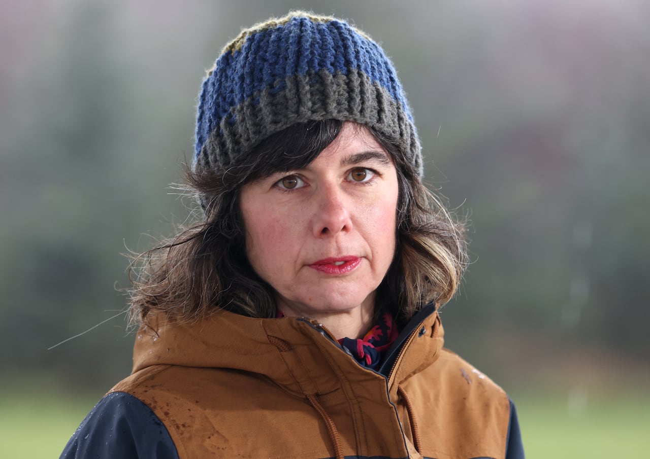 A woman in a winter jacket and toque sitting on a picnic table.