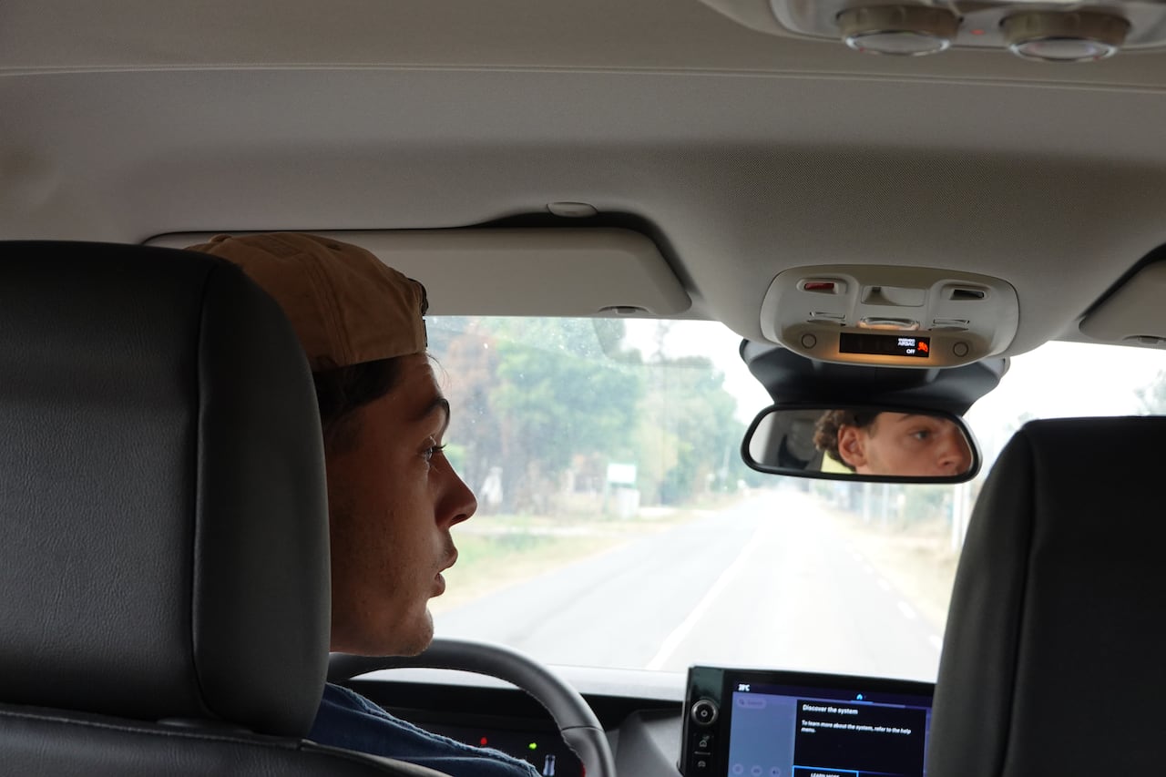 A young man is seen inside a car, driving.