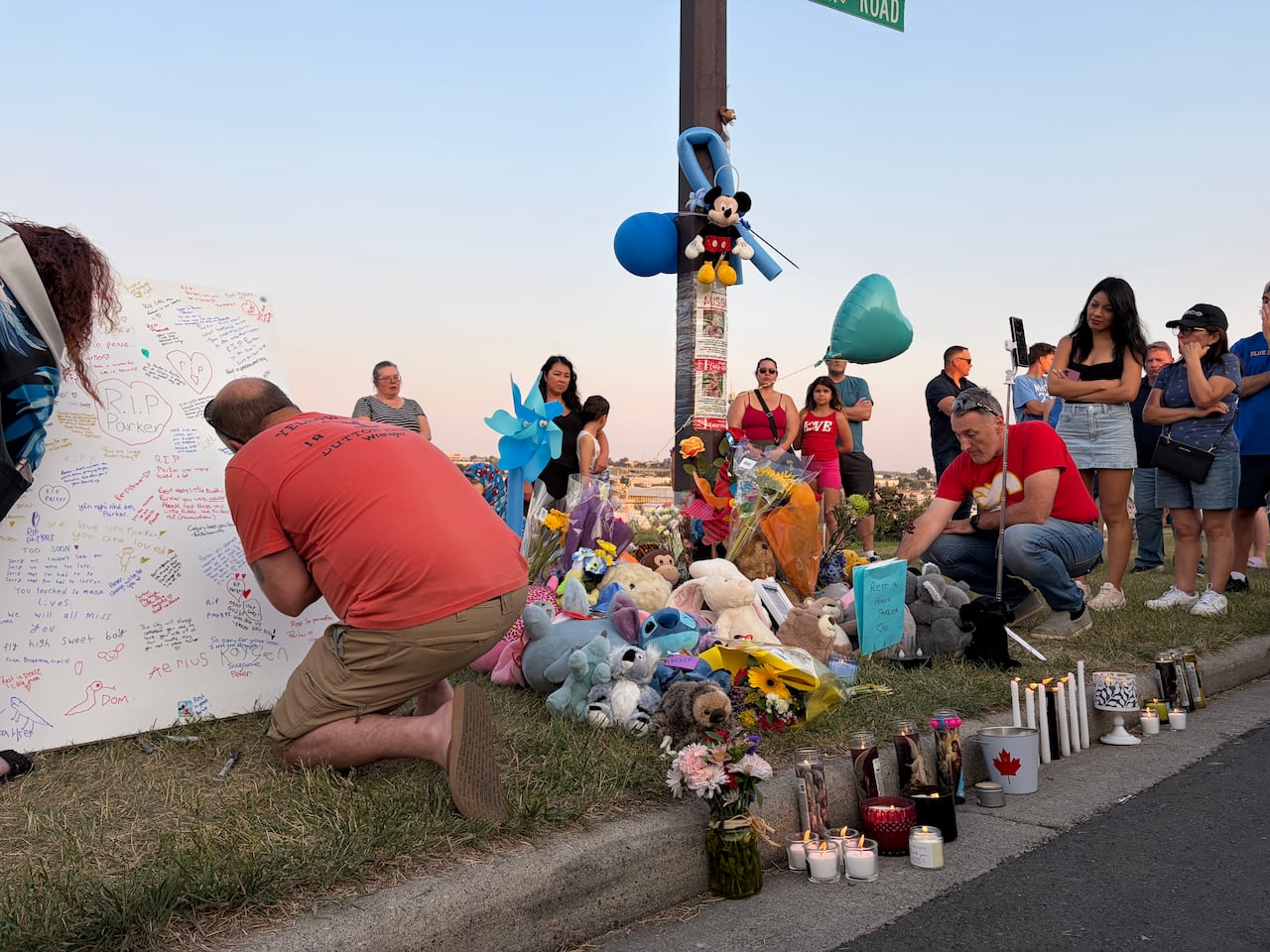 A man kneels in the foreground to sign a message board, with stuffed animals piled up next to him.