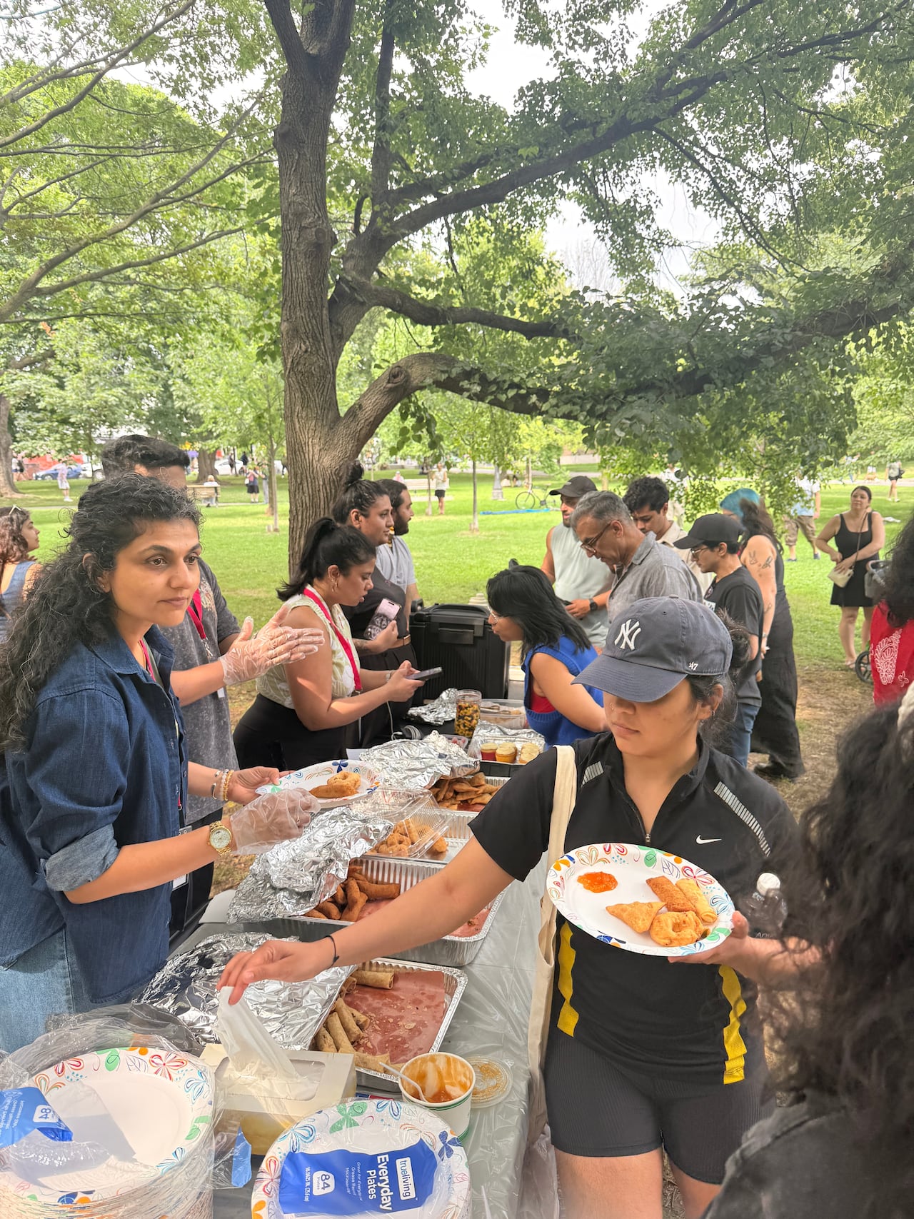 A woman in a hat takes food from a community buffet table.