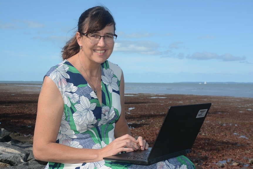 Dr Eva Plaganyi-lloyd working on a laptop, by the sea.