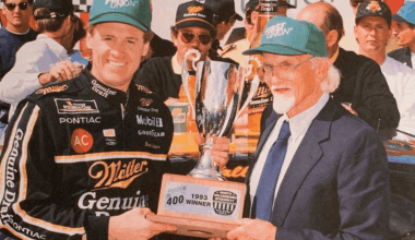 NASCAR driver in a black Miller Genuine Draft suit poses with a large trophy as an older man in a suit presents it at a victory celebration, 1993 First Union win plaque visible on the base.