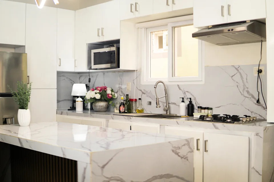 Modern kitchen with marble countertops, white cabinets, stainless steel appliances, and a vase of flowers near a window
