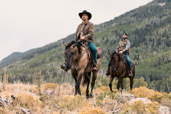 Piya Wiconi Luke Grimes as Kayce Dutton and Logan Marshall-Green as Pete Calvin in Marshals, riding horses through a mountainous landscape.