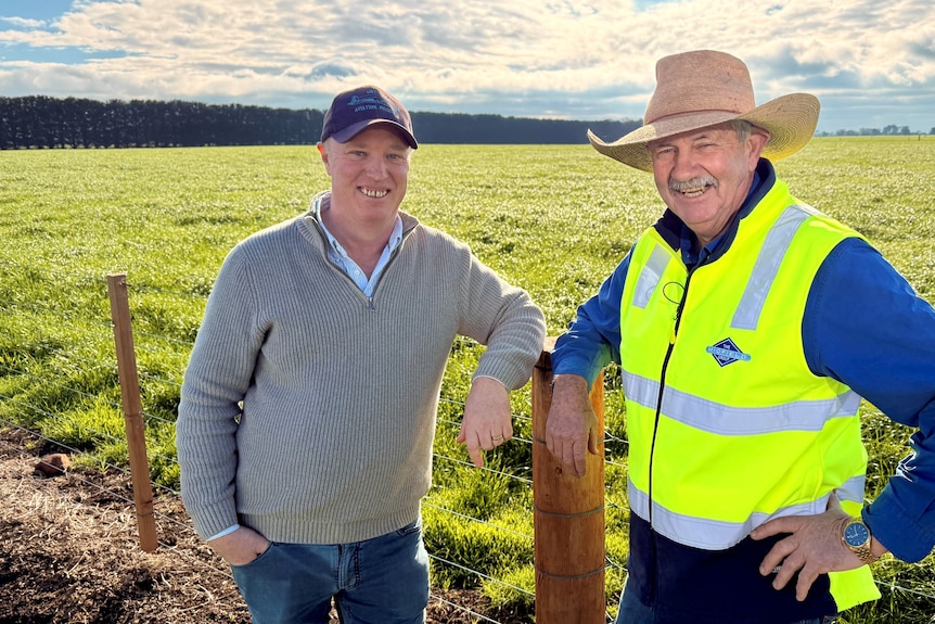 Two men smiling standing in front of a field.