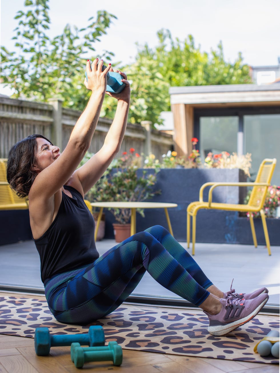 person exercising outdoors with dumbbells raised overhead.