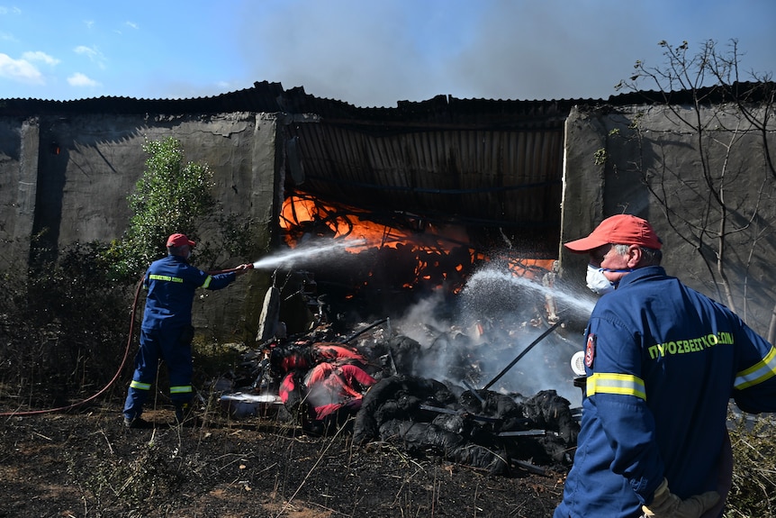 two firefighters spray water onto a building on fire that has partially collapsed