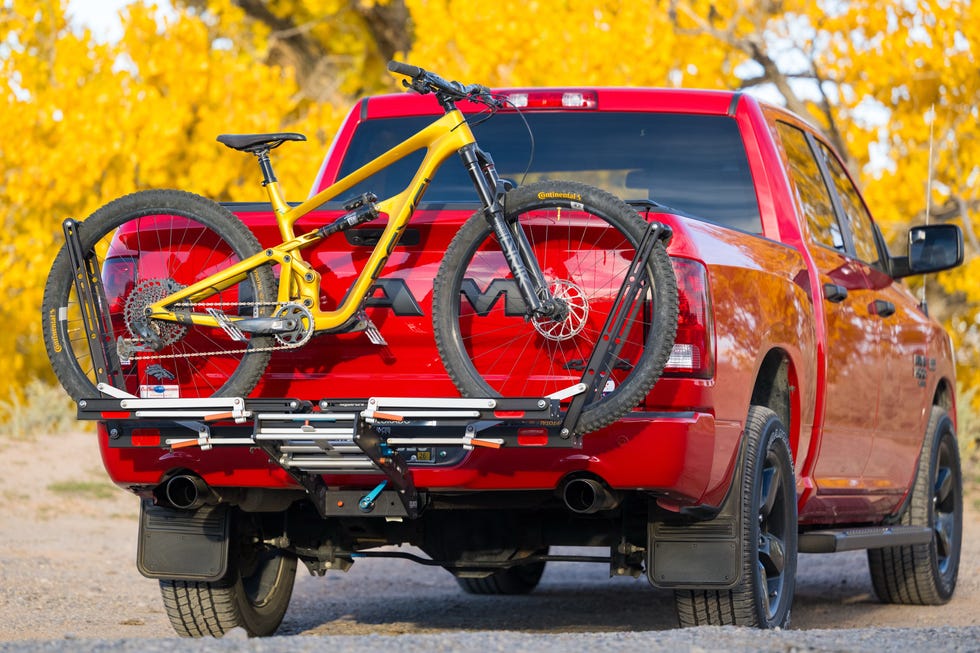 A red pickup truck with a yellow mountain bike mounted on a bike rack, surrounded by vibrant autumn foliage. A red pickup truck with a yellow mountain bike mounted on a bike rack, surrounded by vibrant autumn foliage.