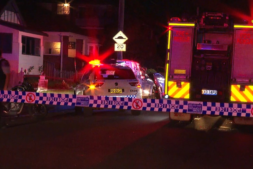 Police cars and a fire engine with lights blaring on a street cordoned off by police tape.