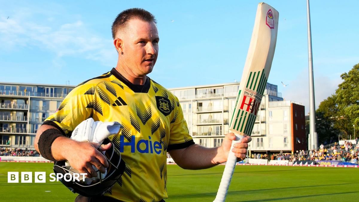 Gloucestershire's D'Arcy Short walks off the pitch at the The Seat Unique Stadium, Bristol, with his bat raised in his left hand and his helmet and gloves under his right arm.