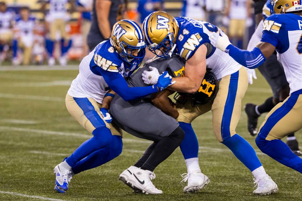 Nick Iwanyshyn / THE CANADIAN PRESS FILES
Winnipeg Blue Bombers teammates Redha Kramdi (left) and Jake Ceresna meet at Tiger-Cats quarterback Tre Ford in Hamilton during Week 5.