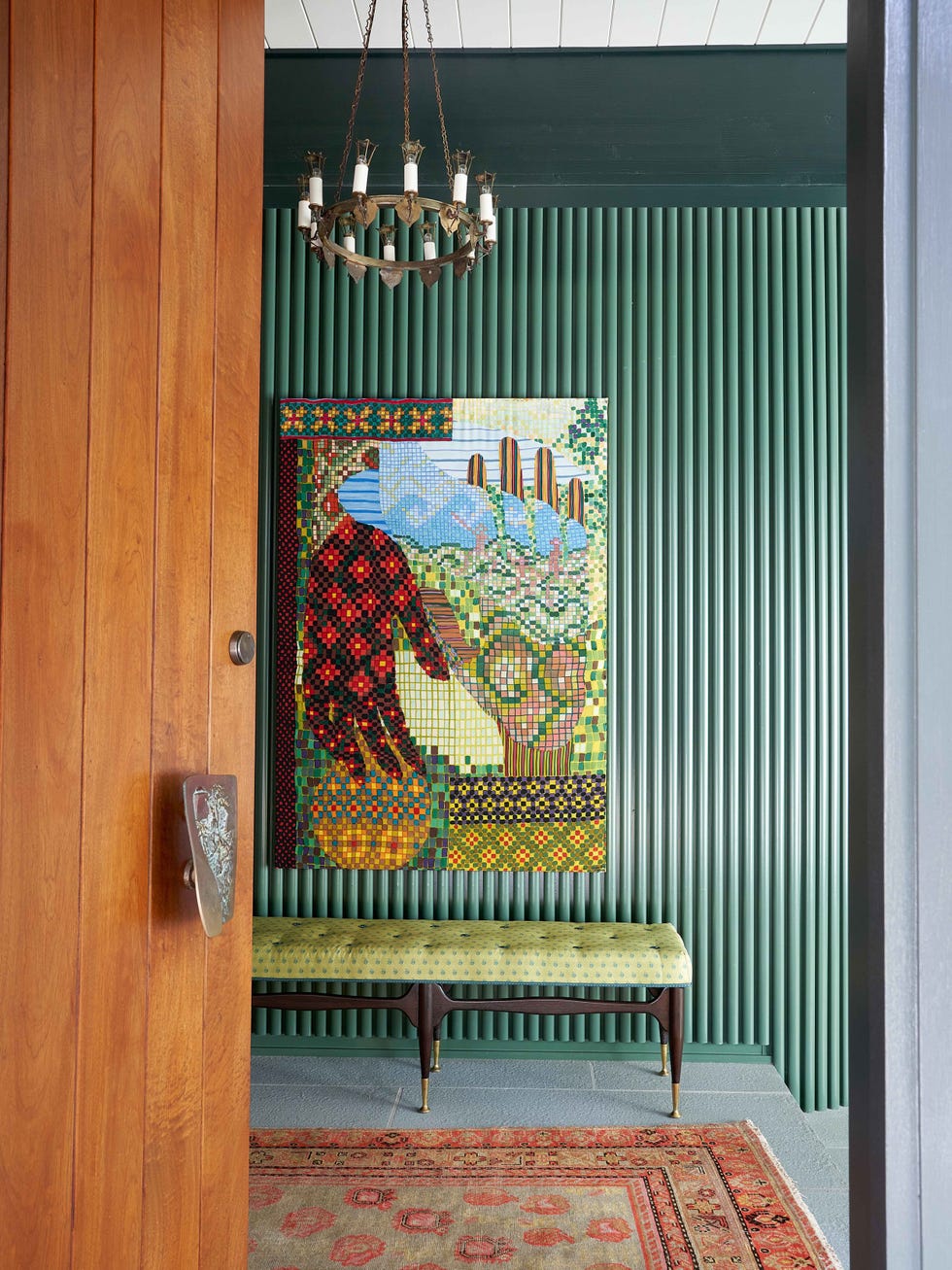 A cozy entryway featuring a colorful mosaic artwork, green striped walls, a patterned rug, and a stylish chandelier.