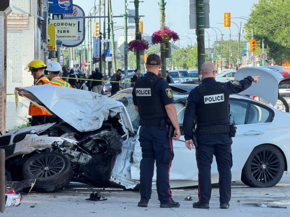 MORGAN MODJESKI / FREE PRESS
Officers with the Winnipeg Police Service survey a crumbled white BMW on Main Street on Friday.