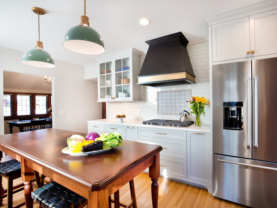 Modern kitchen with a large island, stainless steel fridge, dark range hood, and flowers on the counter creating a welcoming atmosphere