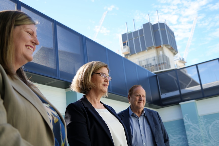 Three people in suits, two women one man, in front of a hospital