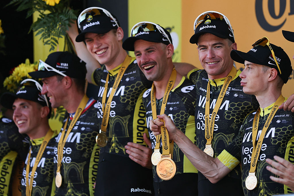 Team Visma | Lease a Bike's Danish rider Jonas Vingegaard (R) tugs on the medal around Team Visma | Lease a Bike's Belgian rider Victor Campenaerts' neck as the whole team celebrates on the podium after winning the 1st stage of the 113th edition of the Tour de France cycling race, a 19 km team time trial stage in and around Barcelona in northeastern Spain, on July 4, 2026. (Photo by Anne-Christine POUJOULAT / AFP)