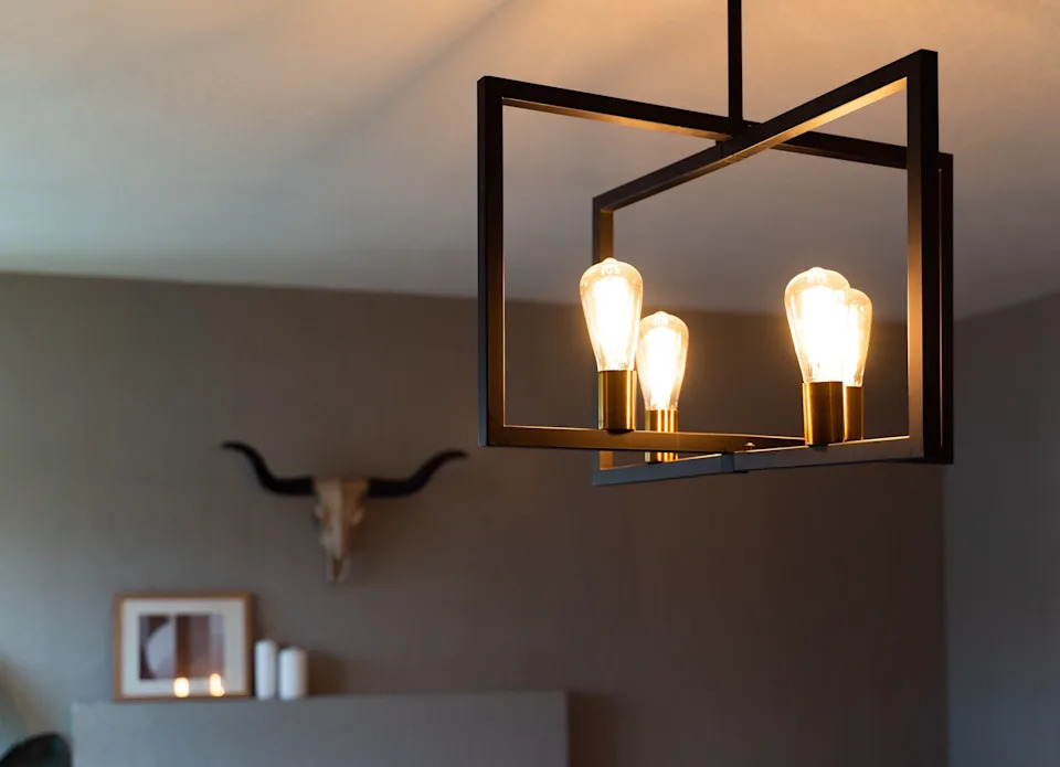 Modern ceiling light fixture with exposed bulbs, casting warm light in a stylish room featuring art and a decorative skull on the wall