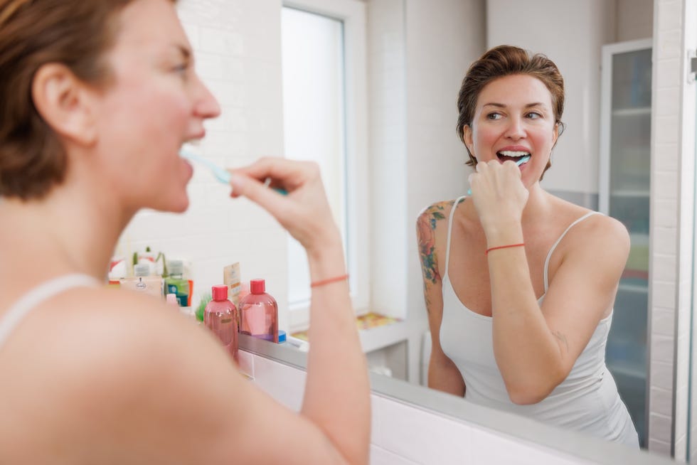 healthy brain ageing habits: woman brushing her teeth in the bathroom mirror