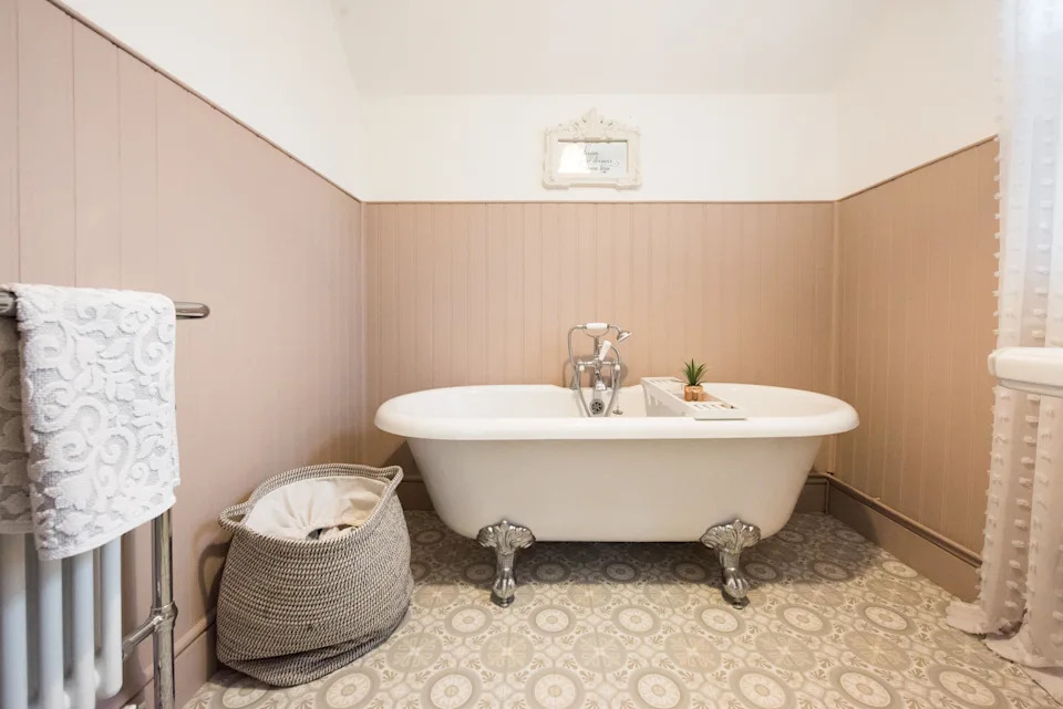 Elegant bathroom with a clawfoot bathtub, patterned floor, and a decorative towel rack. A basket holds towels beside the tub