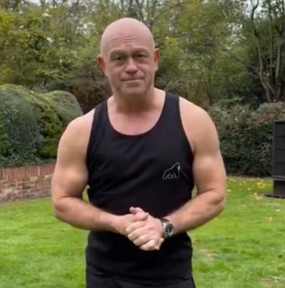 person in black tank top standing on grass with trees in background.