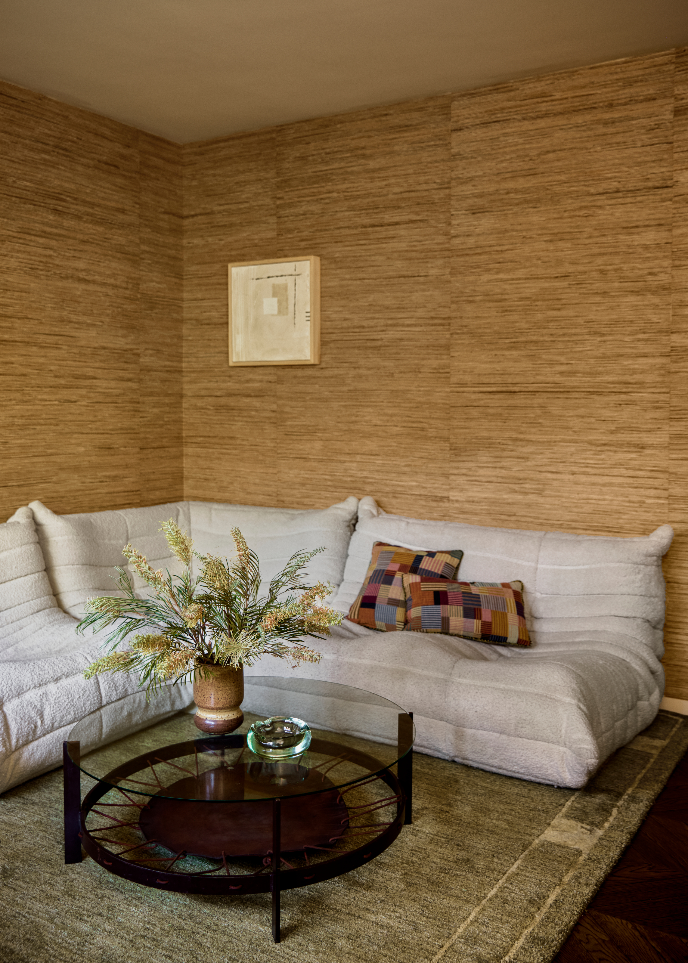 White Togo corner sofa with glass coffee table against a beige-brown grasscloth wallpapered wall