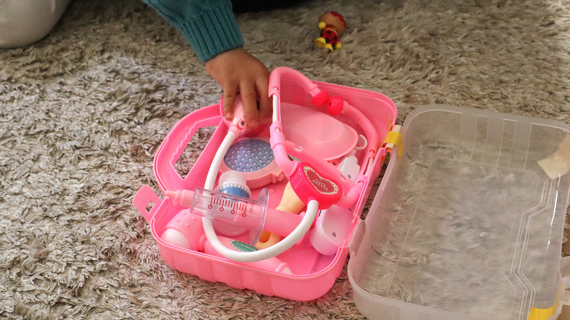 a child's hand reaching for toy doctor's kit containing various medical tools depicted in bright pink plastic