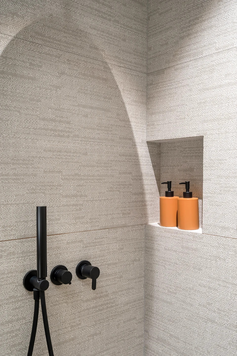 Modern shower with black fixtures and niche, holding two soap dispensers